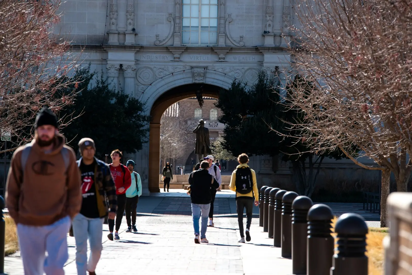 Students walking through a stone archway into a sunlit campus quad