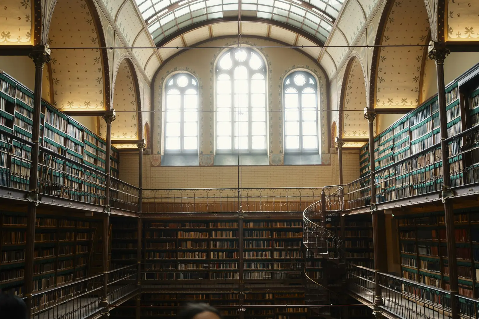 A grand library reading room with tall bookshelves and arched windows