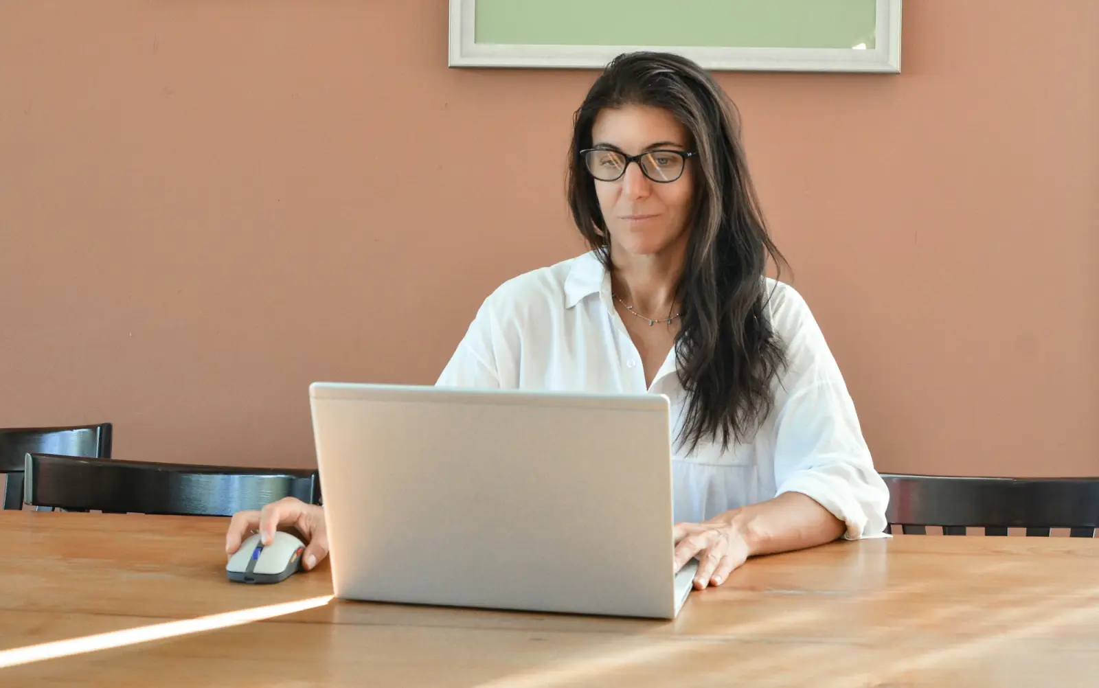 A woman in glasses working on a laptop at a bright desk