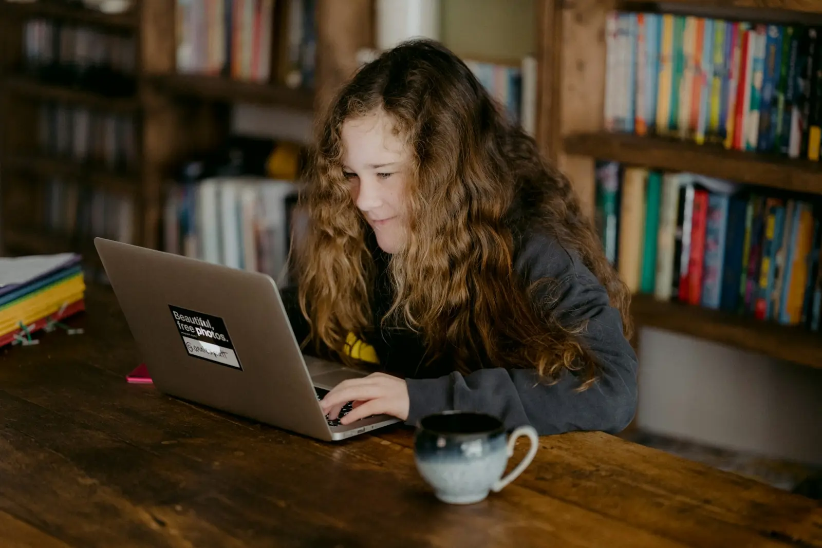 A student working on a laptop surrounded by bookshelves